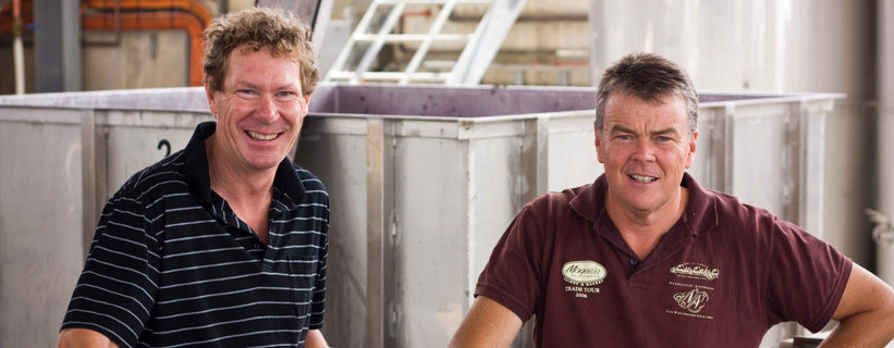 Winemakers and founders Nick Walker (left) and David O'Leary in front of a stainless steel tank at our Clare Valley winery in 2010. Both are smiling and David has one hand on his hip.